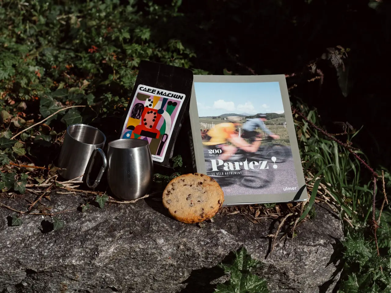 Tasses, café Machin et livre Partez ! posés sur un rocher