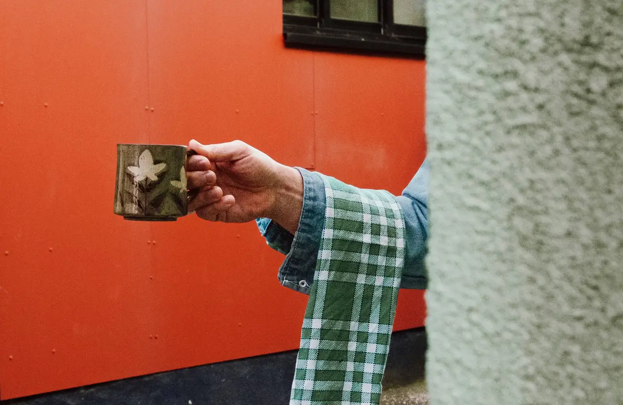 Main tenant une tasse de café devant un mur orange